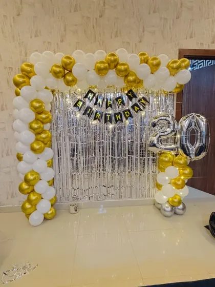 An elegant 20th birthday backdrop with a gold and white balloon arch, a silver tinsel curtain, and '20' in large silver foil balloons.