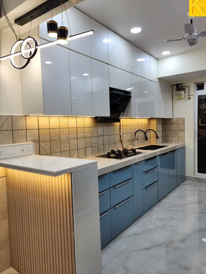 This is a real-site photograph of a parallel modular kitchen we delivered. It features a dual-tone acrylic finish with powder blue and white cabinets, a breakfast counter with fluted paneling, and under-cabinet lighting for a functional and stylish cooking space.
