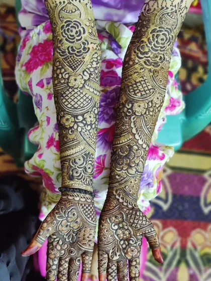 Both arms are covered in a symmetrical design featuring classic floral and checkerboard patterns, a hallmark of Indian bridal mehndi.