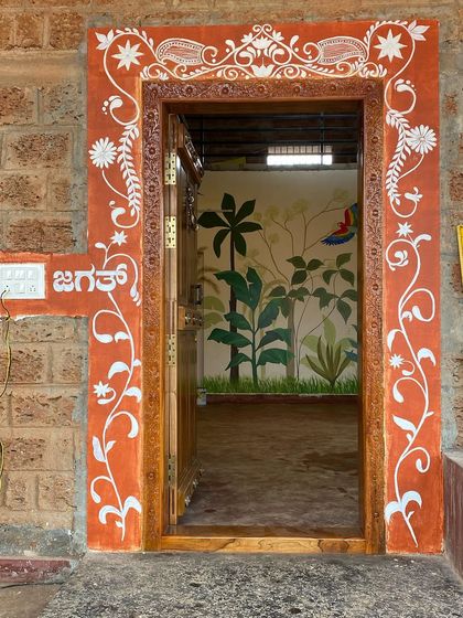 We painted a traditional free-style rangoli design around this stone and wooden door frame. The earthy red color and white patterns create a beautiful, rustic, and welcoming entrance.