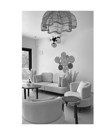 A black and white composition of a living area, showcasing the balance between the curved sofa, round armchairs, and the organic patterns of the wall decor.