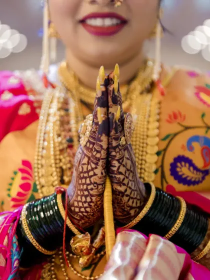 A close-up of the bride's hands in a traditional gesture of greeting (namaste), highlighting her beautiful henna and gold jewelry.