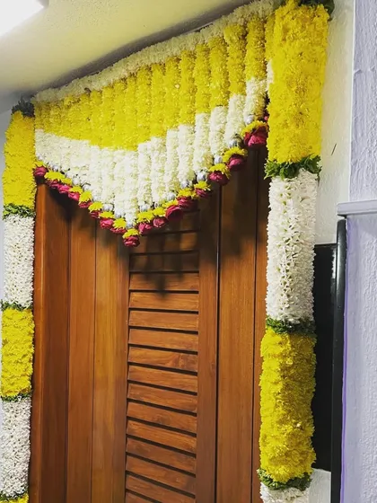 A festive floral decoration framing a wooden door, using garlands of yellow and white flowers.