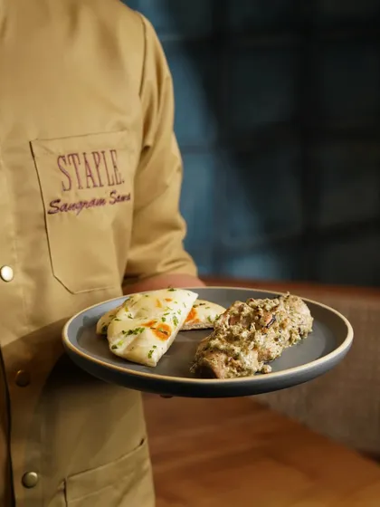 A server presenting a plate of creamy malai chicken with naan. This shot adds a human touch and a sense of hospitality to the dining experience.