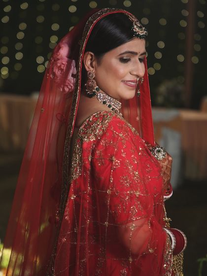 A classic bridal portrait showing the bride in her beautiful red wedding lehenga, with a soft, happy smile.