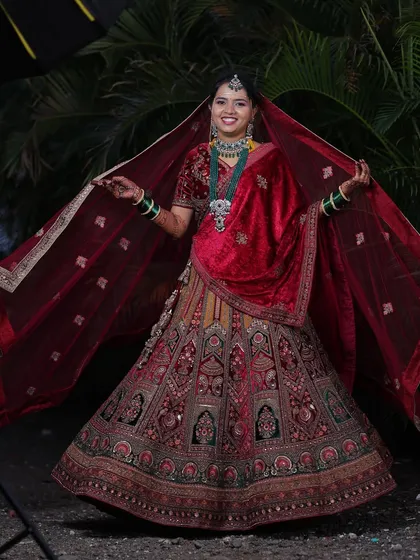 A joyful bride twirling in her stunning wedding lehenga. The rich red velvet and intricate embroidery are captured beautifully in this outdoor shot.