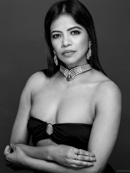 A classic black and white portrait showcasing a diamond and emerald choker. The focus is entirely on the model's expression and the intricate jewellery.