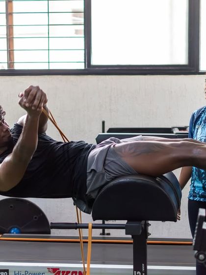 A female coach supervises a client during a challenging glute-ham raise with band resistance. This demonstrates our commitment to building posterior chain strength, which is crucial for power and injury prevention.