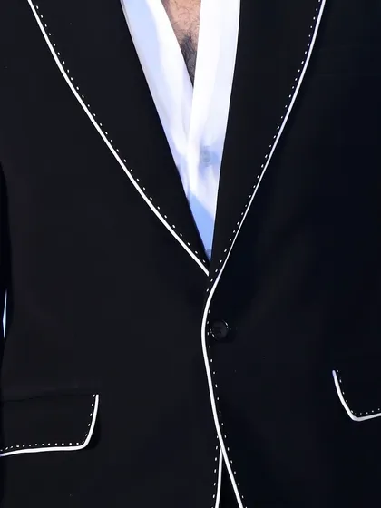 Detail of the lapel and pocket on the custom black suit. The hand-stitched appearance of the white piping adds a touch of artisanal craftsmanship.