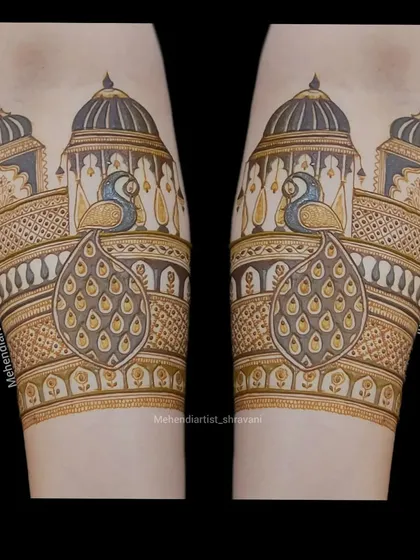 A clean and bold forearm design. This piece highlights symmetrical peacocks sitting on top of royal jharokhas, perfect for a majestic bridal look.