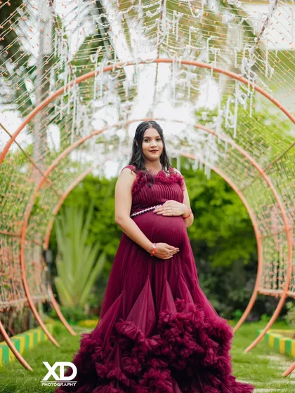 A beautiful solo portrait of the mother-to-be in a maroon gown, standing in a tunnel of lights.