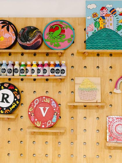 Our pegboard wall is an ever-changing gallery of inspiration. It displays a mix of finished projects, from monogram plaques to pour paintings, and also holds some of our most-used paint colors.