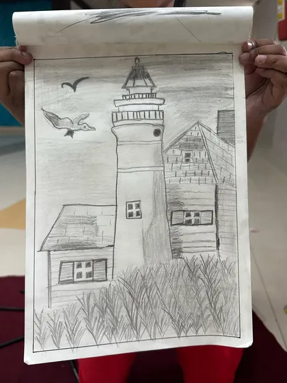 A student holds up their finished drawing of a lighthouse. A great piece from our basic pencil shading lessons.