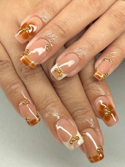 A modern French manicure with a caramel-colored tip and gold bead accents. This is a unique and stylish take on a classic.