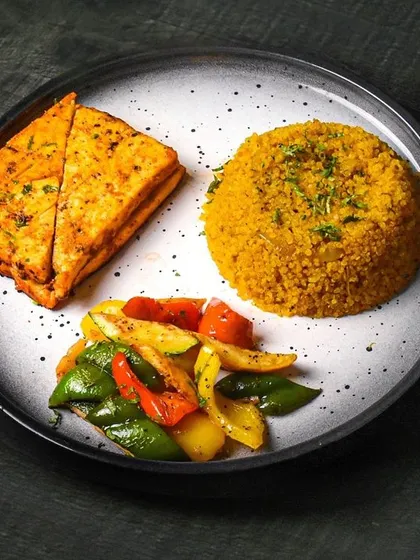 A platter of paneer shish taouk with quinoa and sautéed vegetables. The top-down view on a dark plate creates a clean, modern look for this healthy meal.