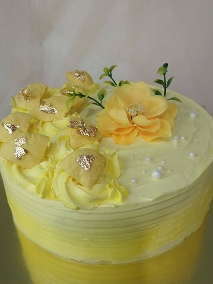 A sunny yellow cake decorated with yellow sugar flowers and gold leaf.