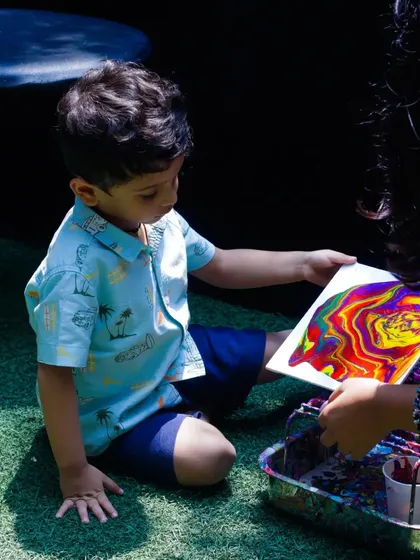 A young boy proudly holds up his finished acrylic pour art at our Father's Day event. The vibrant, marbled colors look incredible, and he was so thrilled with his creation.