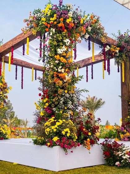 The complete floral mandap, set on a clean white stage that makes the vibrant colors of the flowers pop against the green lawn.