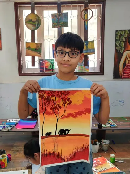 A young artist proudly displays his elephant painting, showing great skill in blending the colours of the sky.