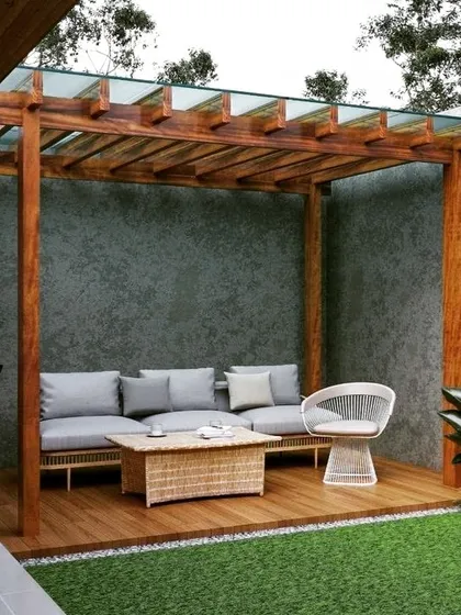 A cozy wooden pergola with a glass-paneled roof, set against a textured concrete wall. The warm tones of the wood deck and wicker furniture create a natural and inviting seating nook.
