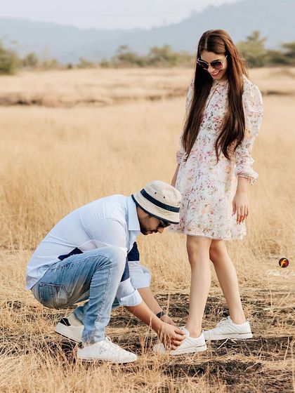 A sweet moment during a pre wedding shoot in a field. The groom tying his bride's shoelace is a small, caring gesture that tells a beautiful story.