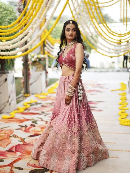 A full-length portrait of the bride at her Mehendi, set against a backdrop of marigold flowers. Her pose is one of grace and confidence.