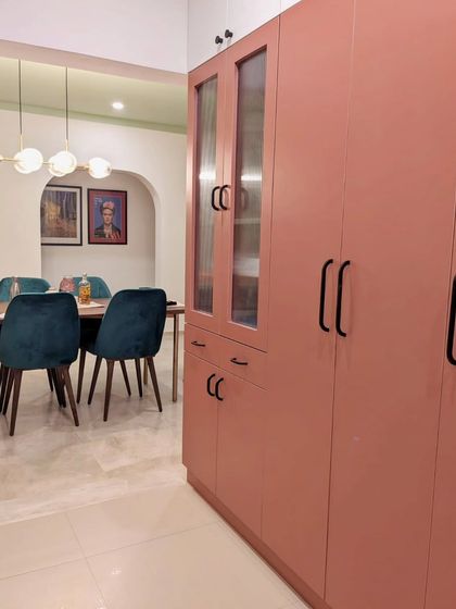 Another view of the pink kitchen, showing its connection to the dining area, which features deep teal velvet chairs. The design is a fun exploration of color and contemporary style.