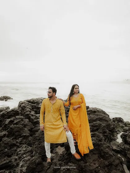 A stylish portrait of the couple standing on the rocks against the sea, their coordinated yellow outfits making a bold statement.