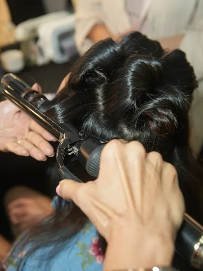 An artist uses a curling iron to create perfect waves. Our hair artistry curriculum covers all the essential tools and techniques for professional styling.