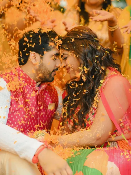 An intimate moment amidst the fun. The couple shares a quiet look as they are showered with marigold petals during their Haldi.