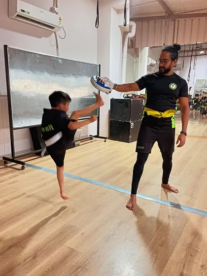 Flying high on a Tuesday. A coach demonstrates a jumping kick, inspiring the students to aim higher.