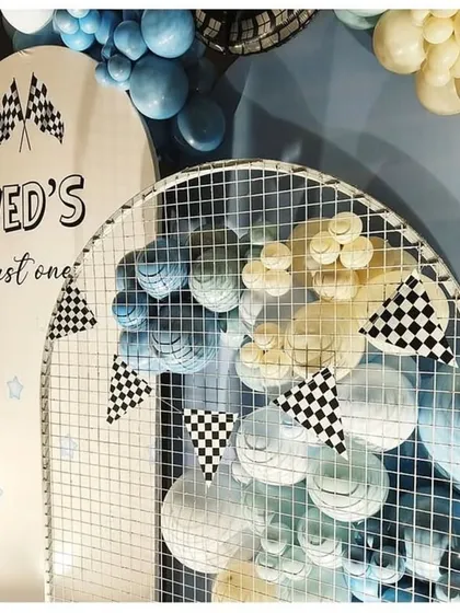 A close-up of the details for "Ved's fast one." The custom arch backdrop with checkered flag pennants and the mesh grid filled with balloons add texture and fun to the race car theme.