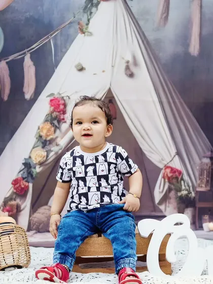 A toddler boy sits in front of a boho teepee for his first birthday photoshoot.
