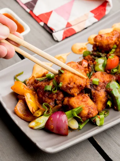 A guest using chopsticks to pick up a piece of our delicious Chilli Chicken, showcasing the tempting texture and fresh ingredients.