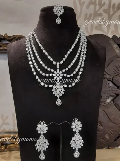 This complete diamond bridal set is designed for maximum brilliance. It features a stunning multi-layered necklace, matching floral-design earrings, and a delicate maang tika, all crafted to create a breathtaking and harmonious look.