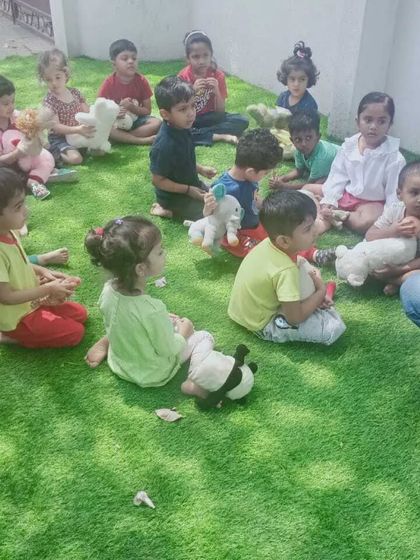 A quiet moment during our Summer Fun Fest. After a morning of activities, the children gathered with their favorite teddy bears for a story, enjoying the fresh air and the company of friends in our green outdoor space.