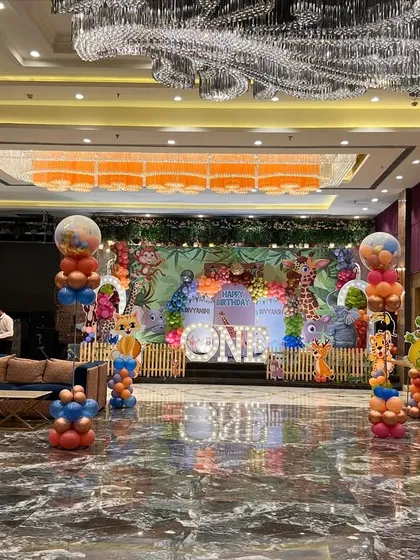 A full view of the banquet hall decorated for a jungle safari party, with themed balloon pillars and table centerpieces.