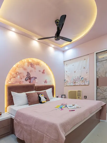 This wider angle shows how the arched headboard, false ceiling with cove lighting, and sliding wardrobe all work together in this pink-themed bedroom.