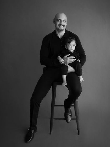 A father and son sitting on a stool for a classic portrait. The black and white treatment gives it a timeless, artistic feel.