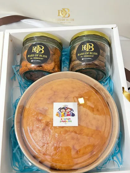 A look inside this Rakhi hamper, showing the large vanilla cake alongside jars of traditional Maida Kaju and classic choco-chip cookies.