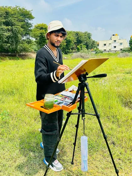 A photo of me painting in a grassy field in rural Bengaluru, fully equipped with my easel and watercolors.