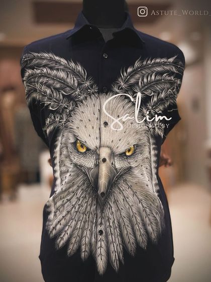 A close-up of a hand-painted eagle on a black shirt. The intense detail and piercing yellow eyes make this a powerful and artistic garment.