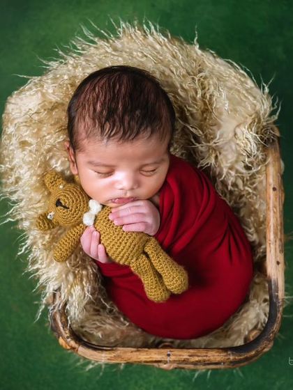 An overhead view of the newborn cuddling a teddy bear, showing the contrast of the red wrap against the green background.