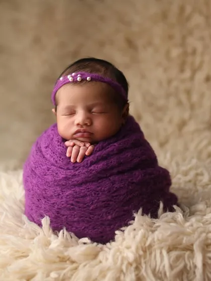 Another variation of the 'potato sack' pose, showing how a simple wrap and headband can create an elegant and beautiful portrait. The focus here is entirely on the baby's serene expression and tiny folded hands.