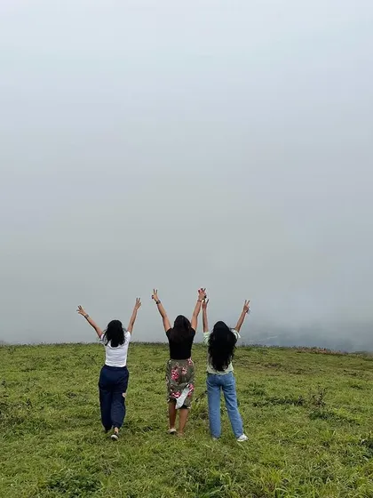 Three travelers celebrating on a misty green hill in Sirsi.
