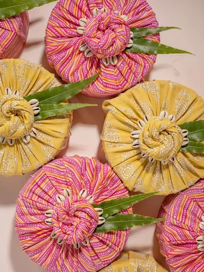 A vibrant flat lay of gifts wrapped in traditional Indian block-printed fabric from Doro. The bright colors and seashell details create a unique and culturally rich visual for festive gifting.