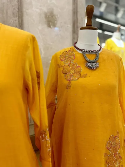 A closer look at the floral embroidered details on this bright yellow kurta, paired with a statement silver necklace for a touch of bohemian elegance.