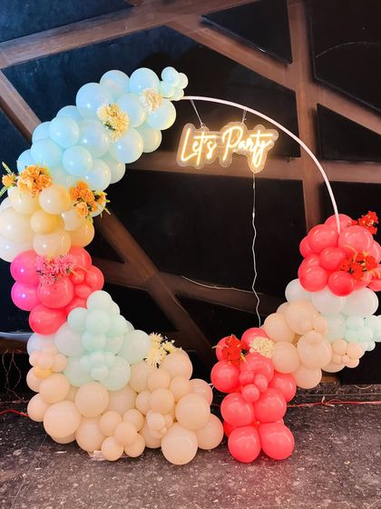 A playful and colorful pastel balloon ring with a 'Let's Party' neon sign. The addition of small flower bouquets gives this design a fresh, summery feel.