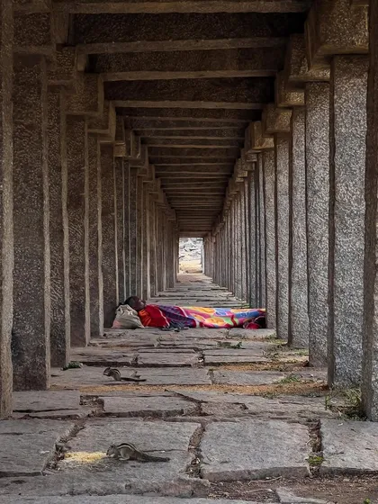 A person sleeps in the long, pillared corridor of a temple, sharing the space with squirrels. This candid shot captures a quiet moment of daily life persisting within the historic ruins.