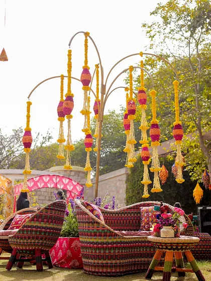 A unique seating arrangement at the carnival, with woven chairs and a tree-like structure adorned with hanging marigold tassels. I focus on creating unique and memorable decor pieces.